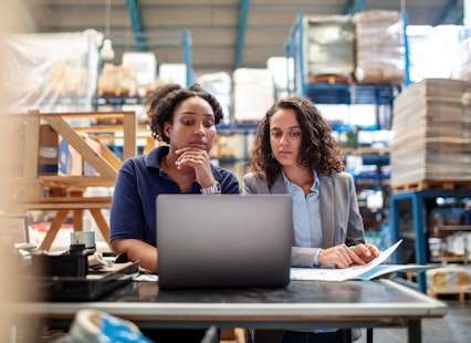 Two young women in a warehouse working on a laptop computer.