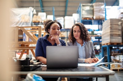 Two young women in a warehouse working on a laptop computer.