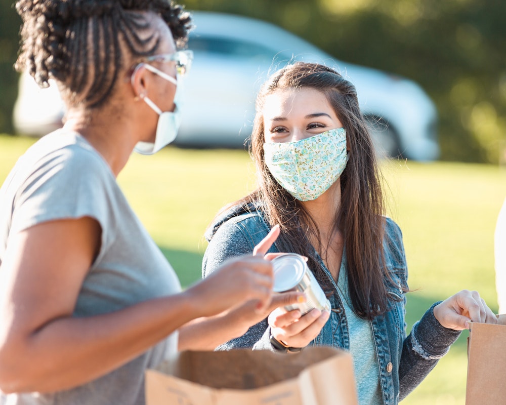 Image of two women in masks during pandemic filling shopping bags with food to help those in need