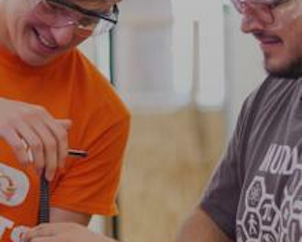 Two students wearing safety goggles and smiling as they hold a tool together