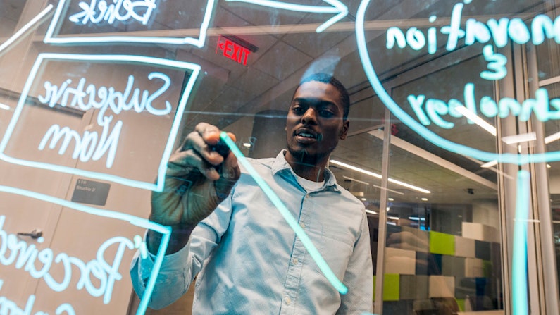 A young adult creating a flowchart with dry erase marker on a pane of glass